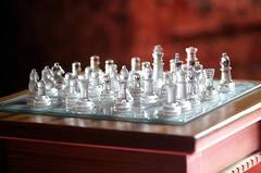 A glass chess set on a wooden table