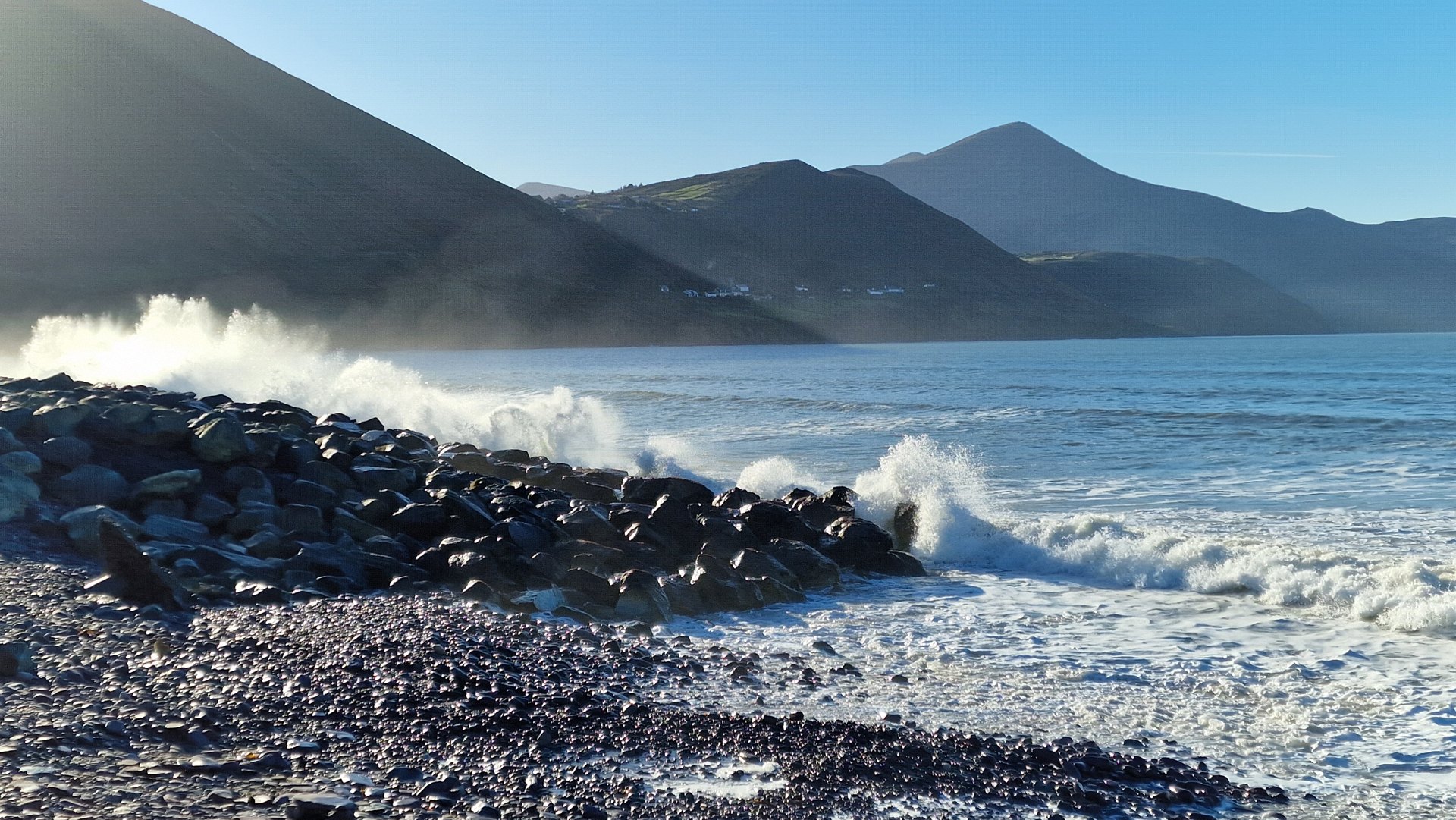 Waves breaking on the stony shore below the mountains on Dingle Bay