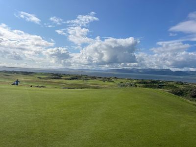 A golf fairway running towards the sea under big clouds