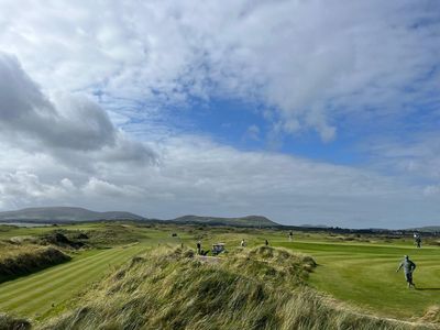 Golfers on a links course among the dunes, with mountains behind