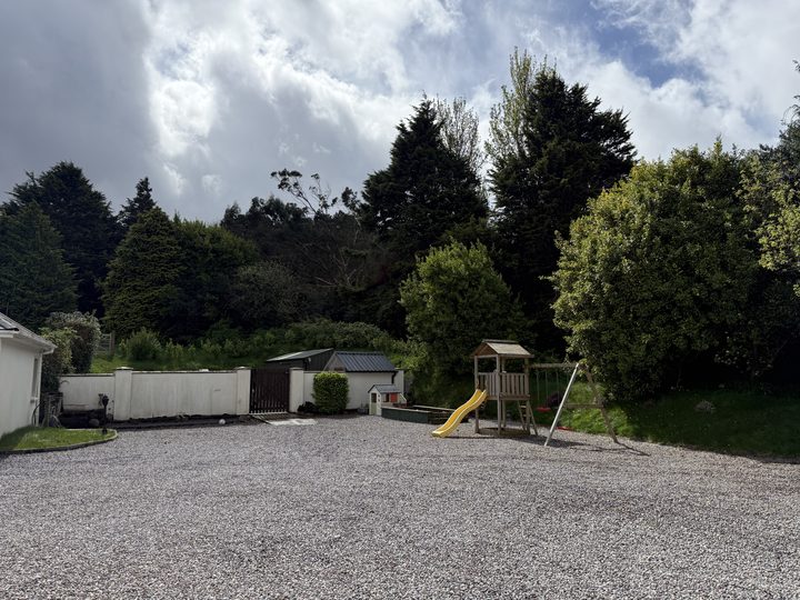 The gravel car park with a children's climbing frame and slide among the trees