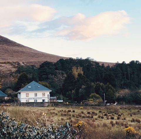 Kerry Ocean Lodge, a white building with a blue roof, below wooded hills in the evening light